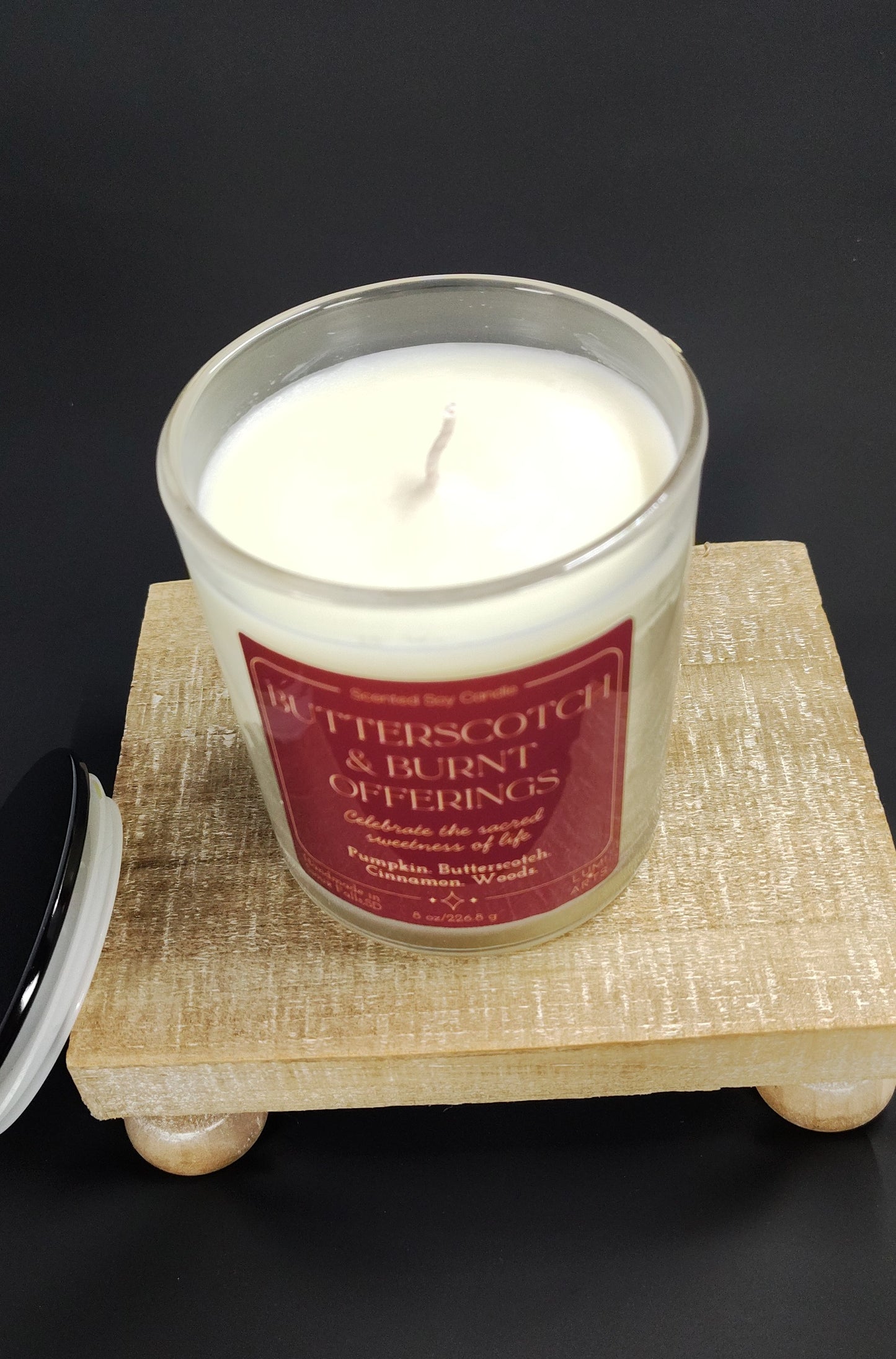 Candle in a glass jar with a red label on a wooden stand against a black background