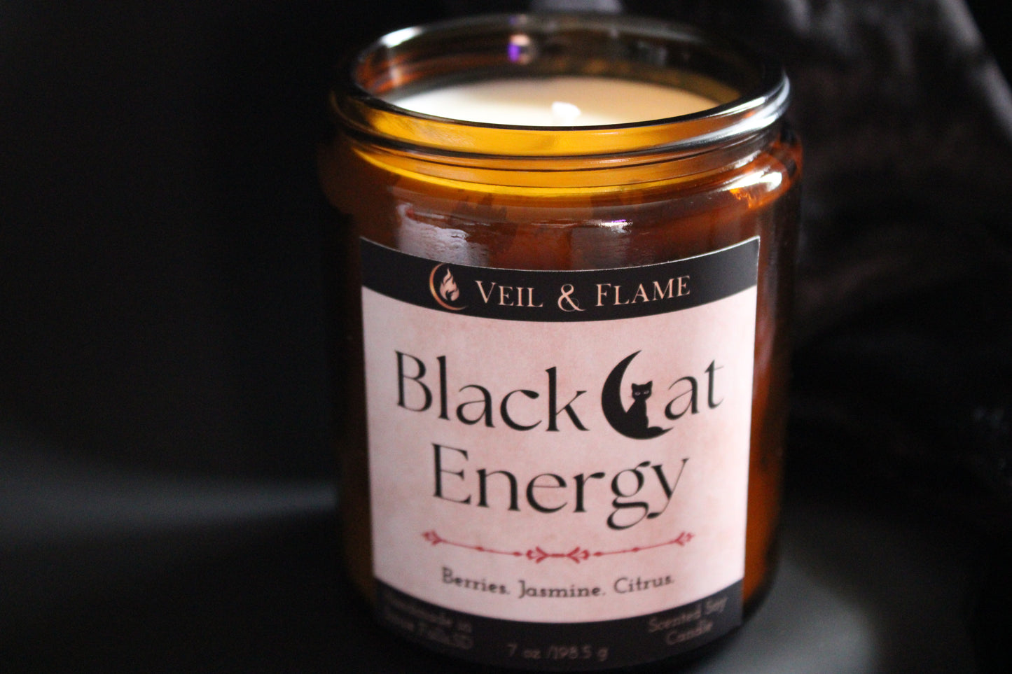 Candle in a glass jar labeled 'Black Cat Energy' by Veil & Flame on a dark background.