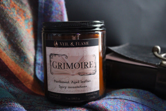 Candle labeled 'Grimoire' by Veil & Flame on a textured fabric background