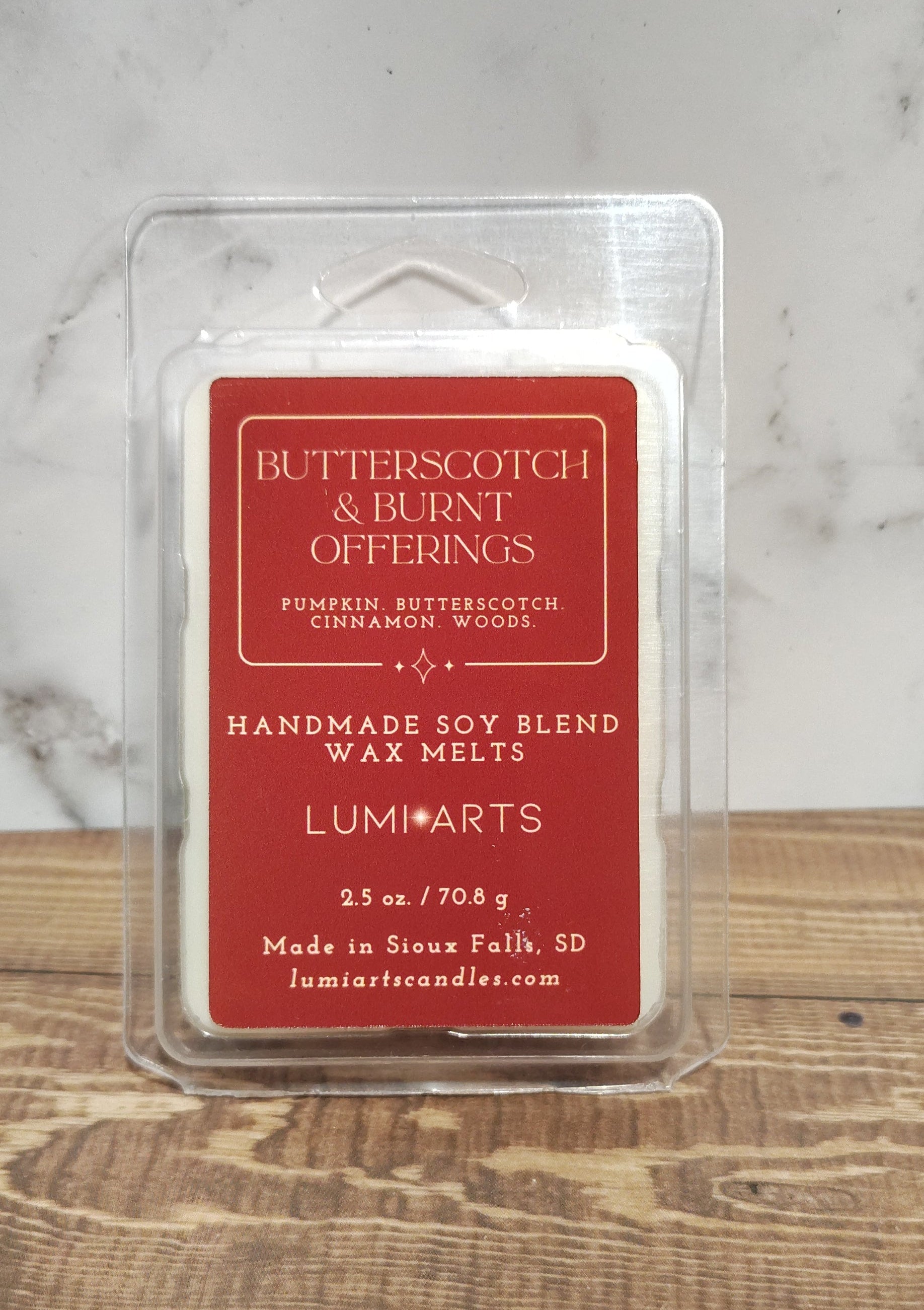 Butterfly Offings wax melt in a clear container on a marble and wooden surface