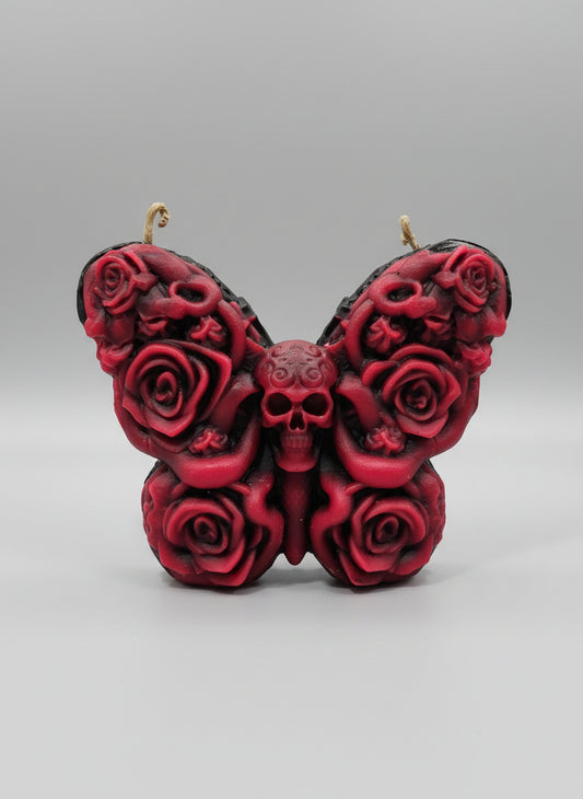 Red butterfly-shaped candle with skull design on a wooden surface