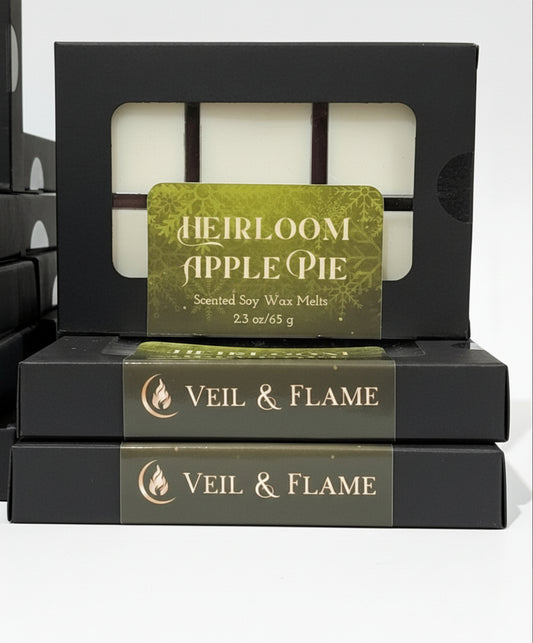 Set of wax melts with visible brand names on a wooden surface. Brand is Veil & Flame. Stacked black boxes of wax melts in apple pie scent. 