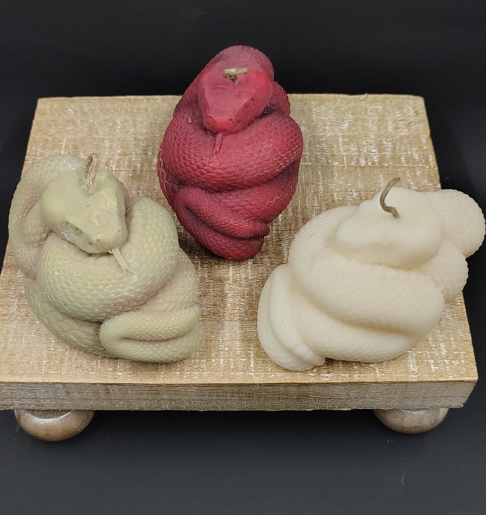 Three skeins of yarn in red, green, and white on a wooden block against a black background.