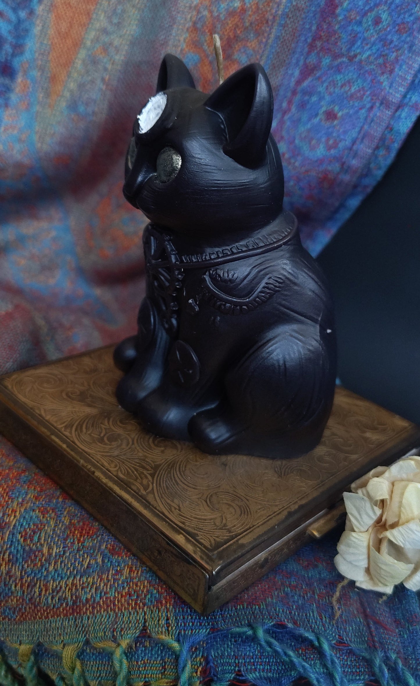 Black decorative cat candle on a wooden stand with a colorful fabric background