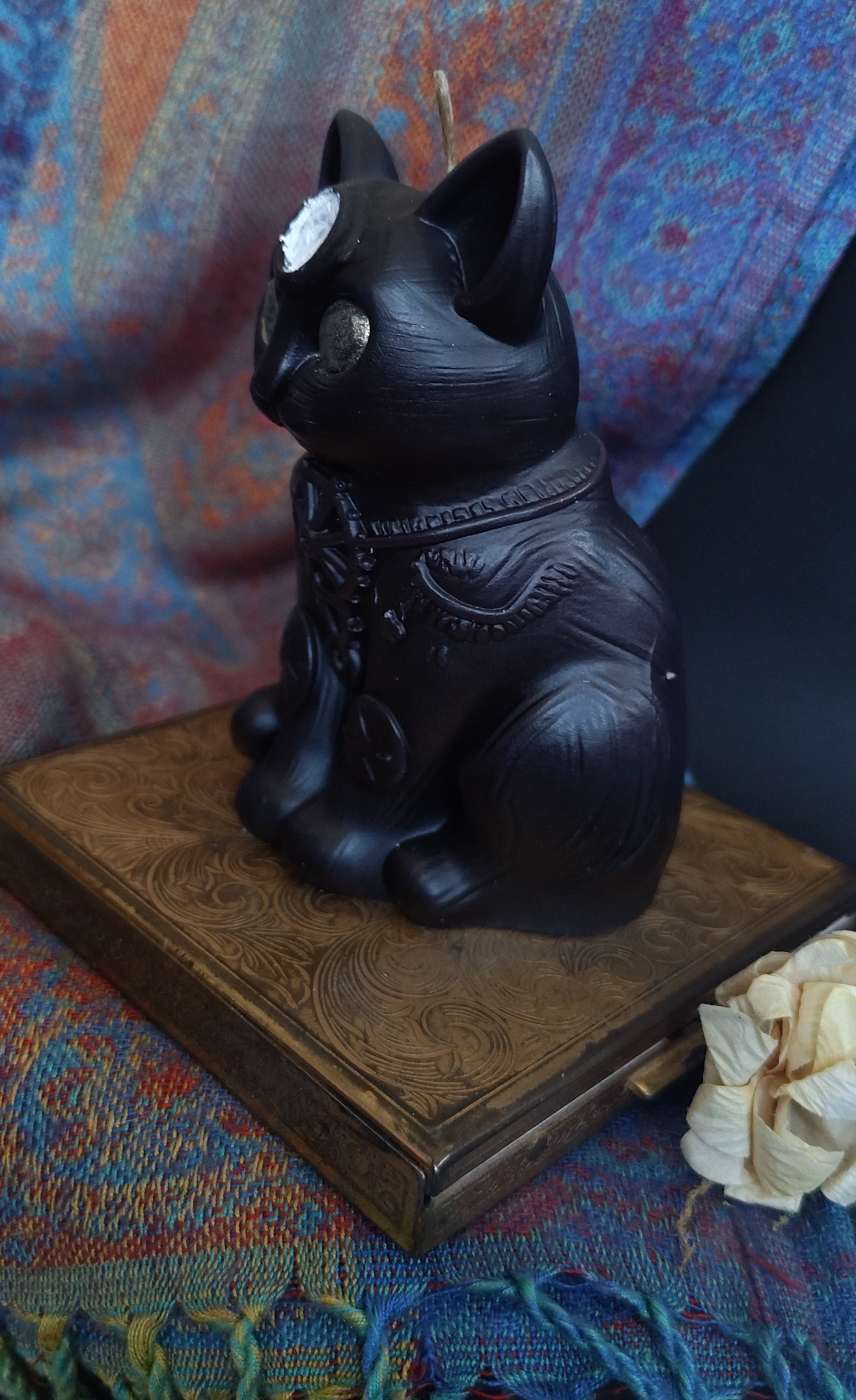 Black decorative cat candle on a wooden stand with a colorful fabric background