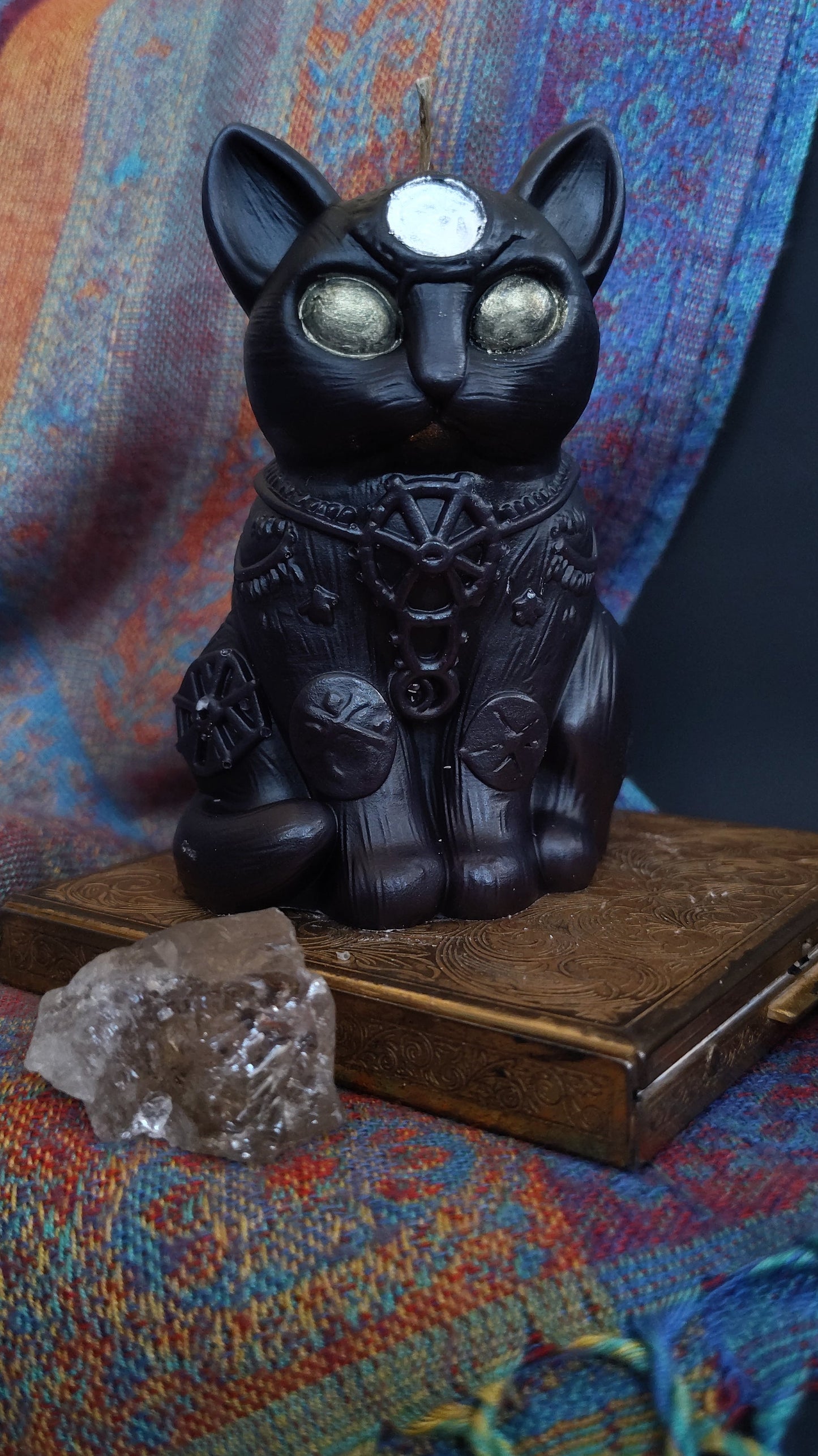 Black cat figure candle with a silver circle on it's forehead, green eyes, and standing on a gold plated case. 