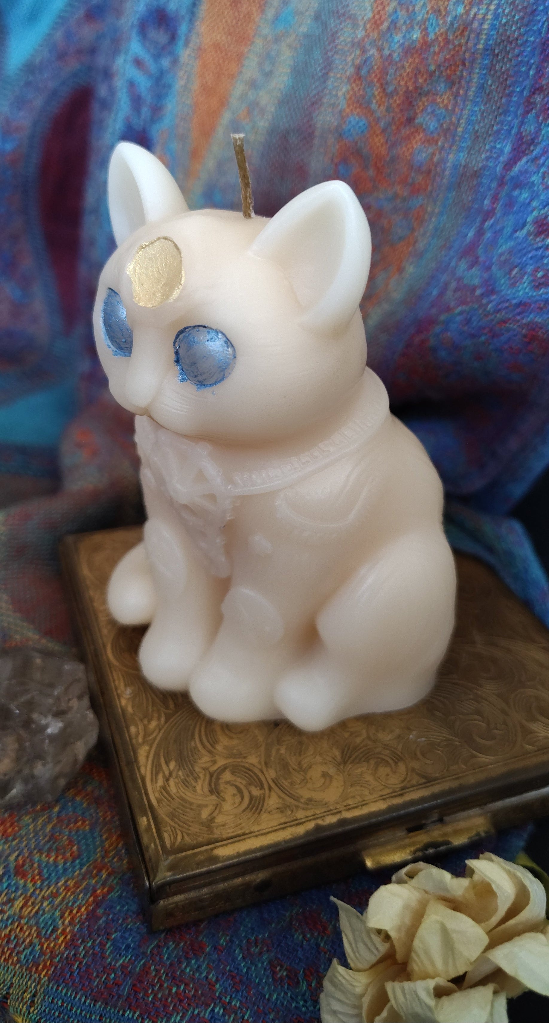Candle shaped like a cat with blue eyes on a colorful fabric background