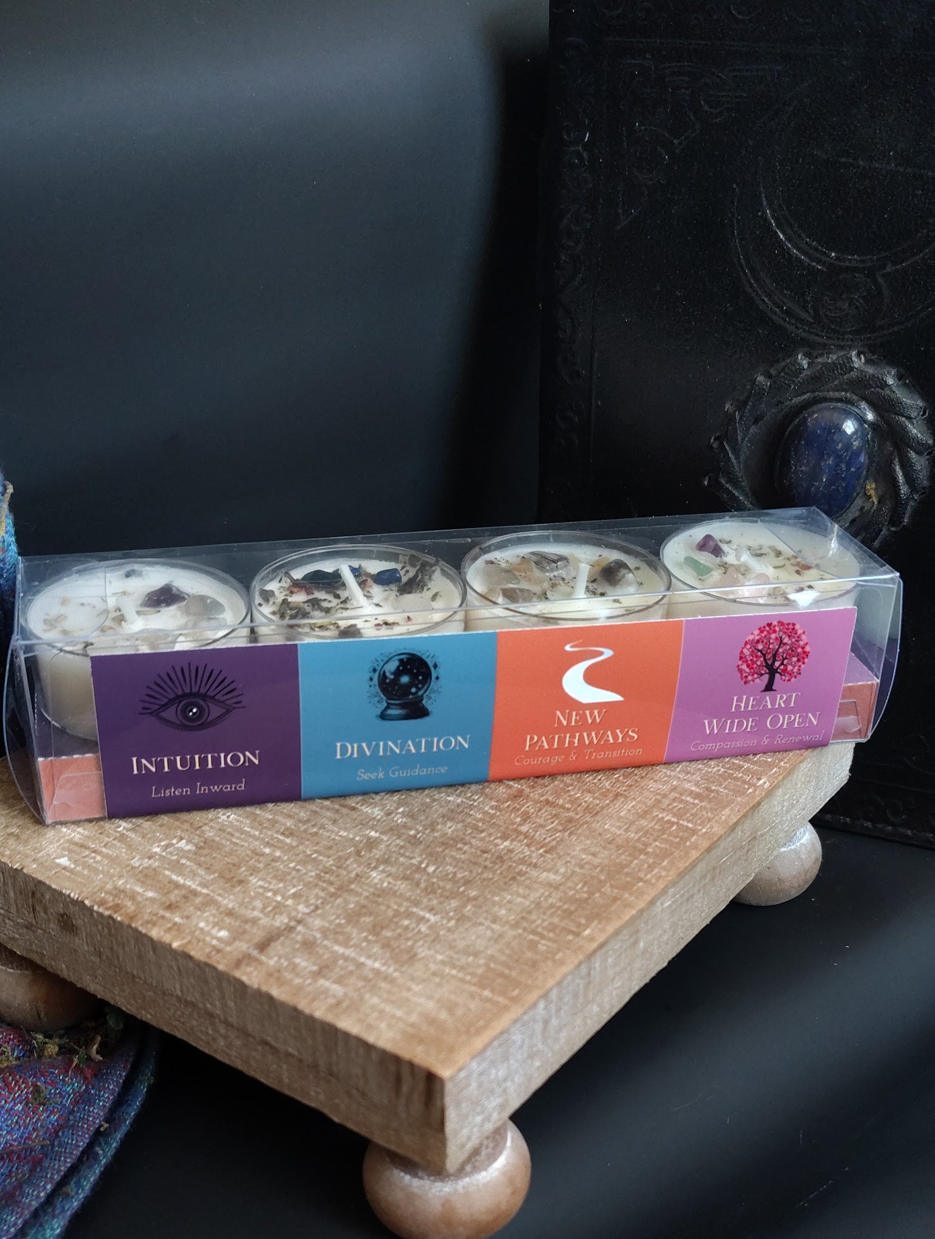 Pack of four small candles in a decorative box on a wooden surface.