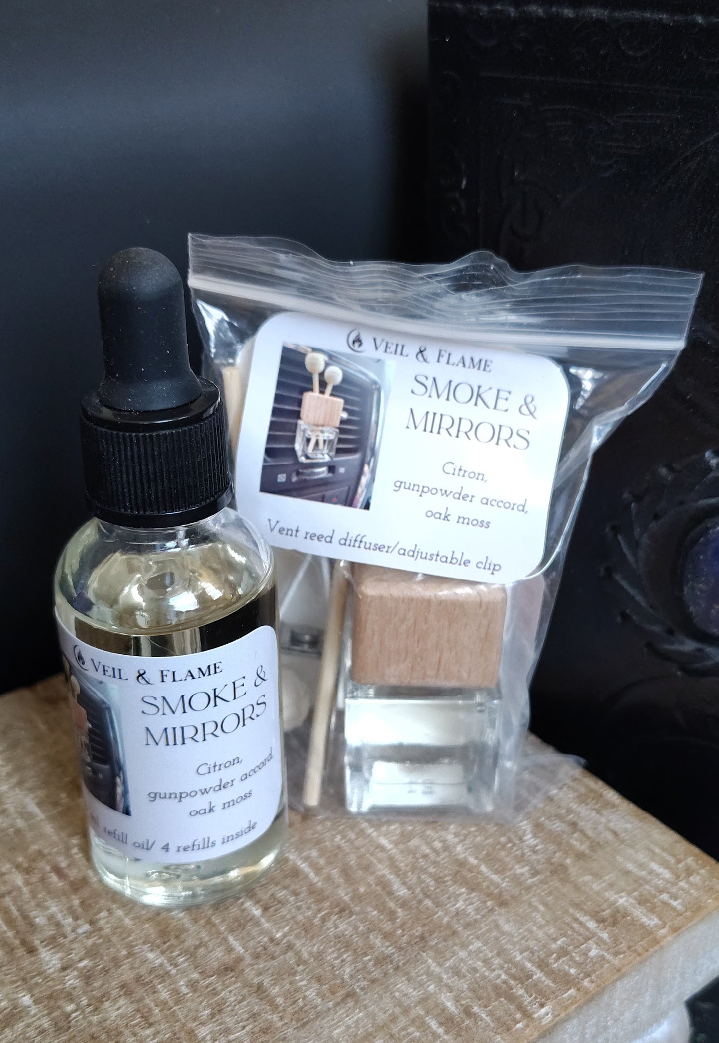 Vee & Flame Smoke & Mirrors diffuser oil bottle and packaging on a textured surface.