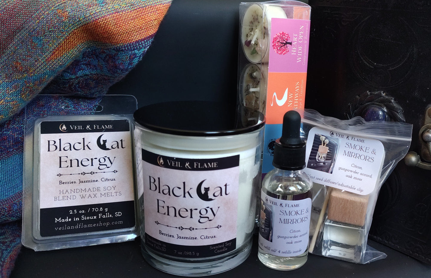 Collection of 'Black Cat Energy' products including a candle, bottle, and packaging on a textured surface.