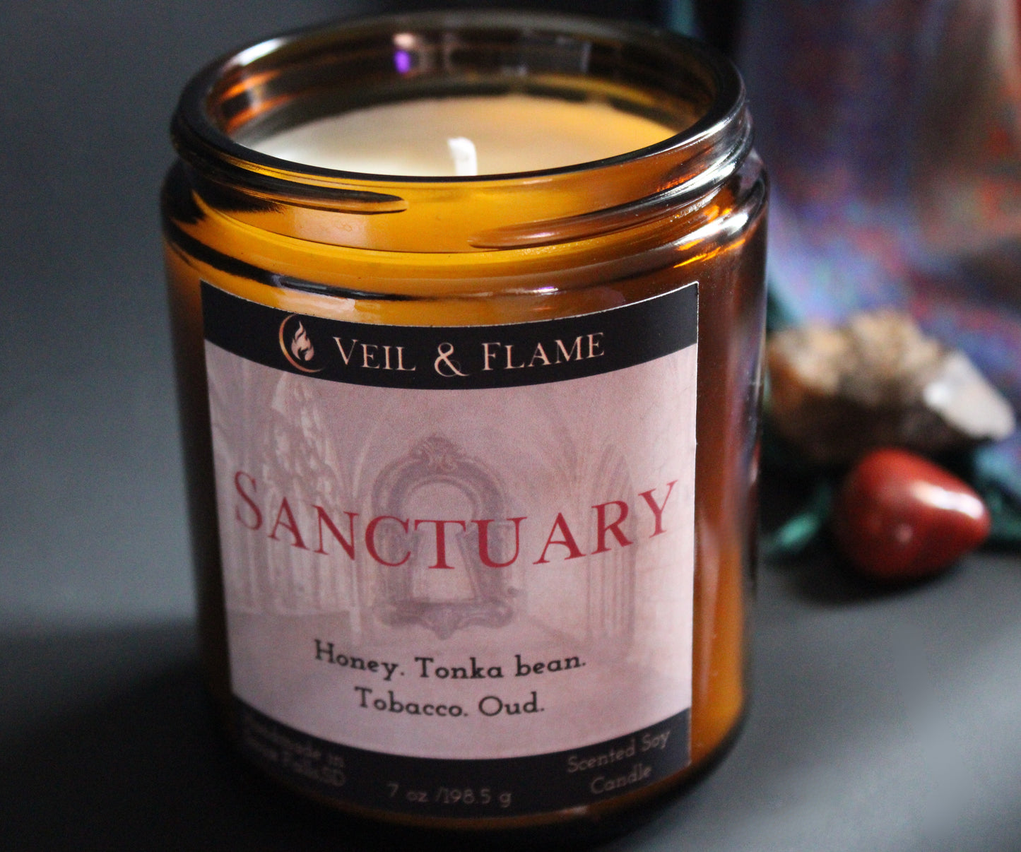 Candle in an amber jar labeled 'Sanctuary' by Veil & Flame on a dark background.